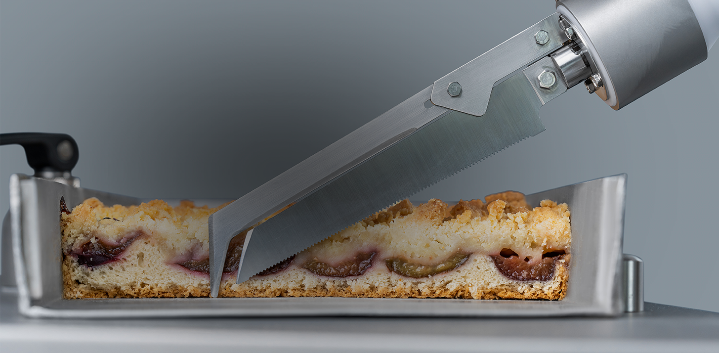 Detailed view of a pneumatic blade lying in front of a sliced plum cake in a tray.